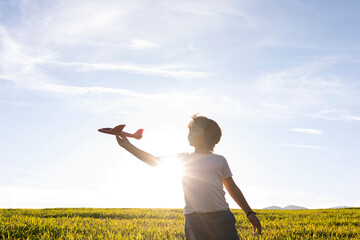 Boy playing with airplane toy while while standing against clear sky