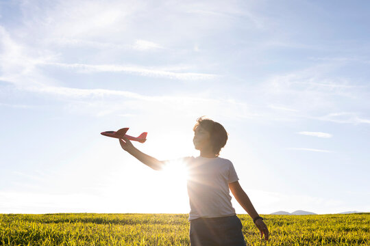 Boy playing with airplane toy while while standing against clear sky