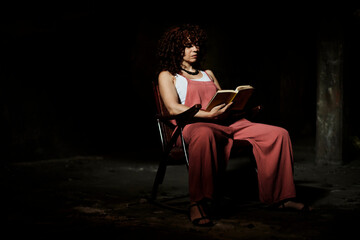 Woman sitting on chair while reading book at dark room