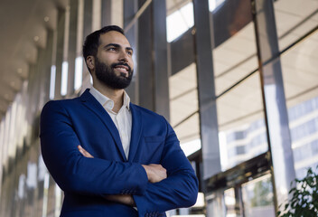 Portrait of handsome middle eastern businessman looking away standing in office, copy space. Young pensive entrepreneur brainstorming,  planning start up project. Successful business