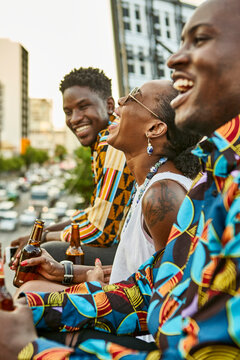 Laughing friends sitting on roof terrace in the city drinking beer, Maputo, Mozambique