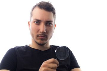Handsome young man with magnifier, selective focus on eyes. Portrait on white background.