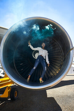 Full length portrait of smiling young woman holding distress flare while standing inside airplane's turbine at airport