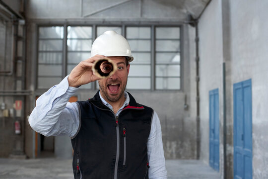 Male architect with mouth open looking through cardboard while standing in building