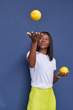 Portrait of happy young woman juggling with two oranges in front of blue background