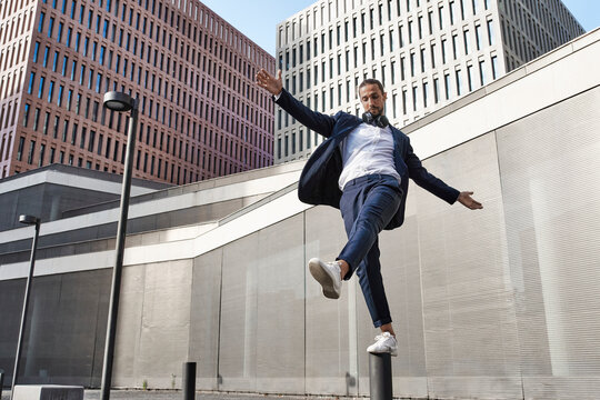 Businessman with headphones balancing on pole against office building