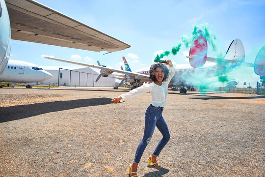 Cheerful young woman dancing with distress flare at airport runway on sunny day