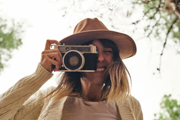 Smiling woman photographing through vintage camera in forest