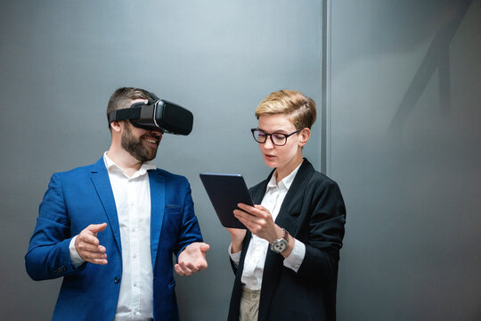 Female entrepreneur using digital tablet while analyzing colleague experiencing virtual reality simulation at office