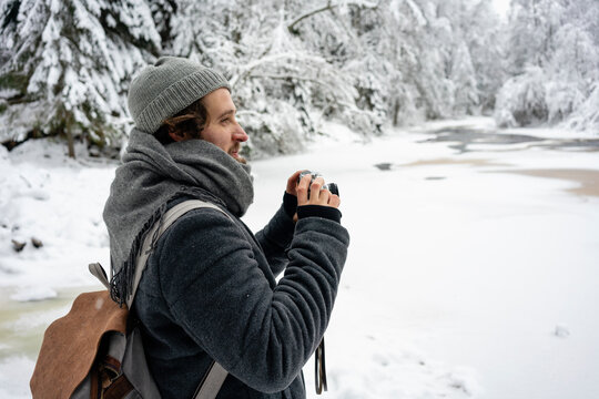 Young man with backpack and camera looking away while standing at forest