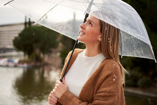 Happy woman looking up while holding umbrella during rainy season