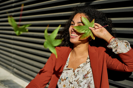 Autumn leaves falling on smiling young woman against shutter during sunny day