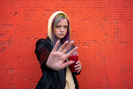Portrait of young woman with dyed hair raising hand in front of red wall