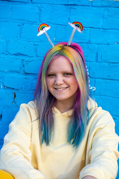 Young woman with dyed hair and rainbow alice band in front of blue wall