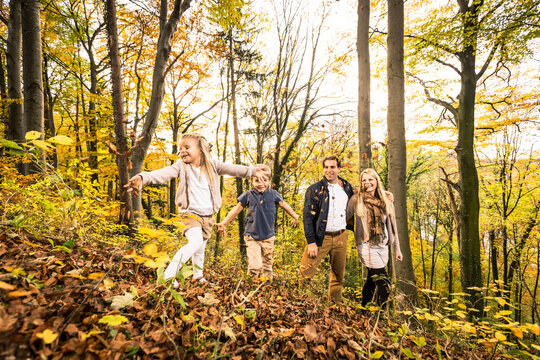 Smiling parents looking at children playing in forest during autumn