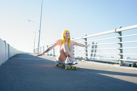 Young woman sitting on skateboard against clear sky during sunny day