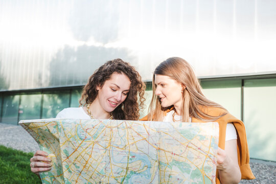 Smiling female friends holding map in city on sunny day