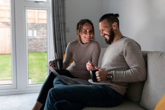 Smiling young couple having tea while using laptop on sofa at home