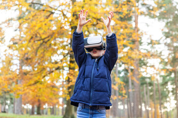 Boy using virtual reality simulator whiles standing with hand raised in forest