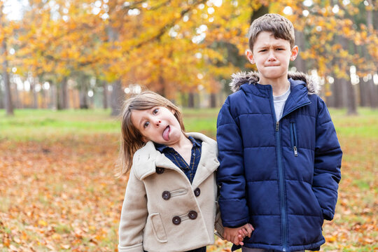 Sibling wearing jacket teasing while holding hands standing in forest