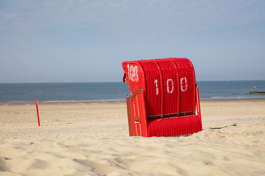 Red hooded chair on sandy beach against blue sky