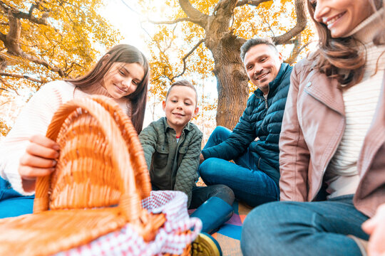 Smiling children opening food basket while parents sitting on picnic blanket in park during autumn