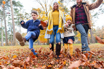 Smiling family playing with fallen leaf while walking in forest