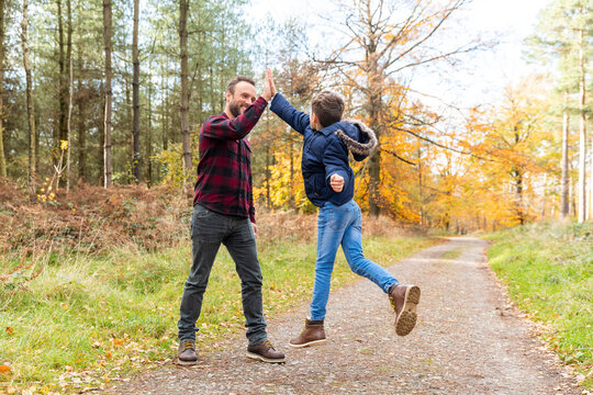 Son jumping while giving high-five to father standing in forest