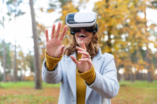 Smiling woman wearing virtual reality headset stretching hands while standing in forest