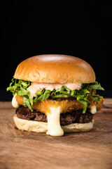 Hambúrguer com queijo provolone a milanesa derretendo em base de madeira com fundo preto