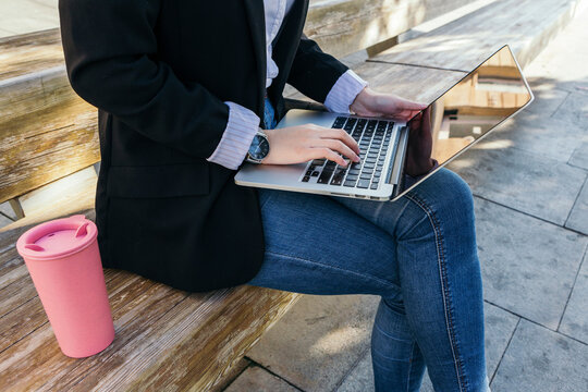 Crop view of young businesswoman sitting on bench outdoors using laptop - Powered by Adobe