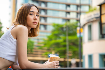 Young beautiful Asian woman holding coffee cup walking down city street and shopping at downtown...