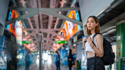 Fototapeta premium Portrait of Beautiful Asian woman tourist waiting for skytrain at railway station platform in the city. Confidence female enjoy city life with outdoor lifestyle travel and shopping at summer time