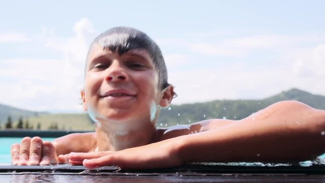 Portrait of shirtless boy getting out of water and leaning on edge of the swimming pool at resort
