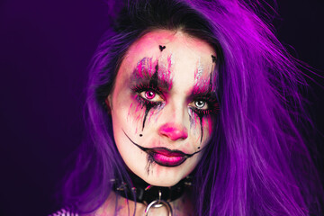 Young woman with scary halloween makeup big eyes colored purple hair and dark background