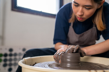  Asian woman sculptor artist hands sculpture clay on pottery wheel at ceramic studio. Female craftsman molding raw clay create pottery shapes at workshop. Small business handicraft product concept.