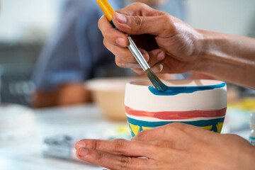 Asian woman learning color painting her self-made pottery at home. Confidence female enjoy hobbies and indoors leisure activity handicraft ceramic sculpture and painting workshop at pottery studio.
