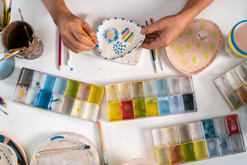 Asian LGBTQ guy learning color painting her self-made pottery at home. Confidence male enjoy hobbies and indoors leisure activity handicraft ceramic sculpture and painting workshop at pottery studio - obrazy, fototapety, plakaty