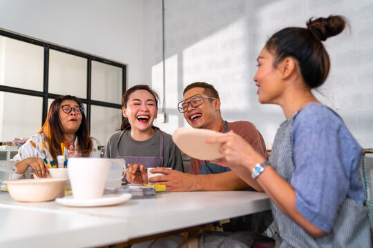 Group of Asian man and woman millennial generation friends enjoy and having fun painting self-made pottery together at pottery studio. Hobbies and leisure activity handmade ceramic painting workshop.
