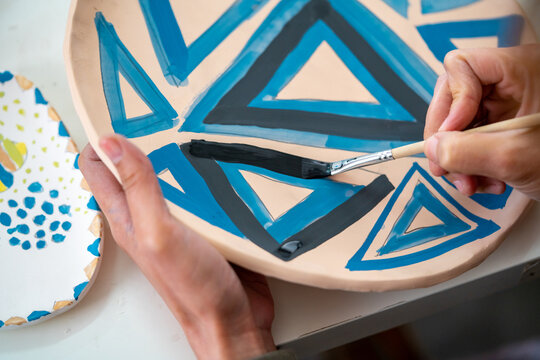 Asian woman learning color painting her self-made pottery at home. Confidence female enjoy hobbies and indoors leisure activity handicraft ceramic sculpture and painting workshop at pottery studio.