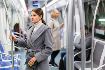 Portrait of focused brunette wearing light overcoat during trip in metro train ..