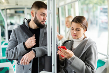 Fototapeta na wymiar Attractive girl and bearded guy using mobile phones in city bus on way to work in fall day