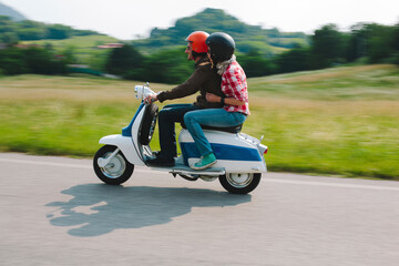 Couple riding vintage motor scooter on country road, Tuscany, Italy