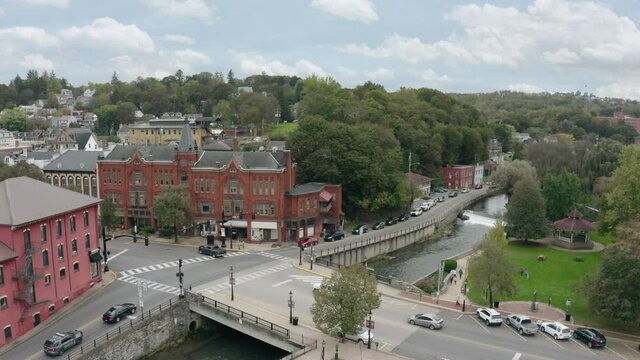 A slow forward-moving aerial establishing shot of the downtown district of Bellefonte, Pennsylvania on an early Fall day. Small park with gazebo below.  	