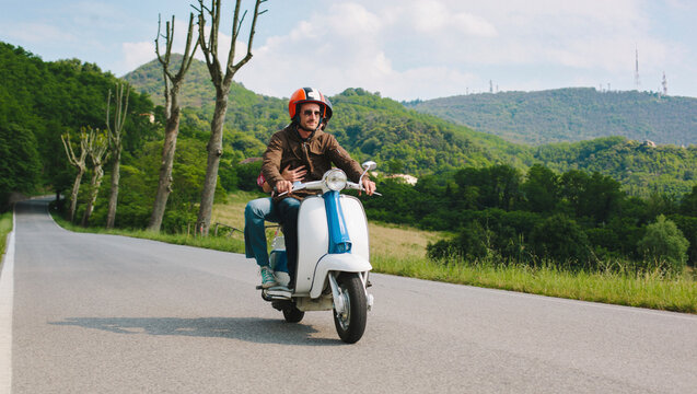 Couple riding vintage motor scooter on country road, Tuscany, Italy