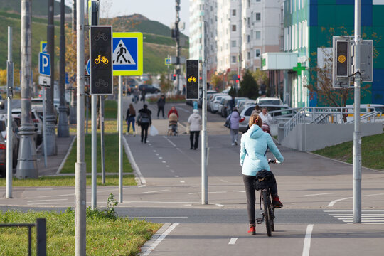 Woman in a blue jacket on a bicycle waits for a green signal for a bicycle traffic light. Blurred image of people walking in a residential area in autumn.