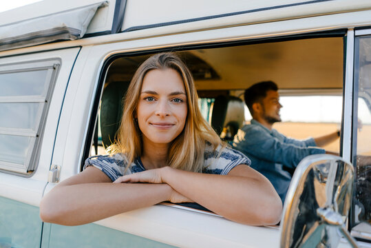 Portrait of smiling woman leaning out of window of a camper van with man driving