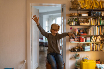 Boy sitting on buck in his room at home wearing cardboard VR glasses