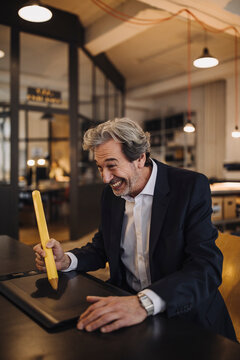 Silly senior businessman with giant pencil at desk in office