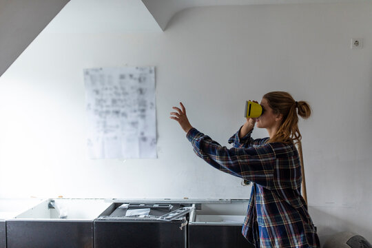 Young woman wearing VR glasses with assembly instructions at kitchen wall